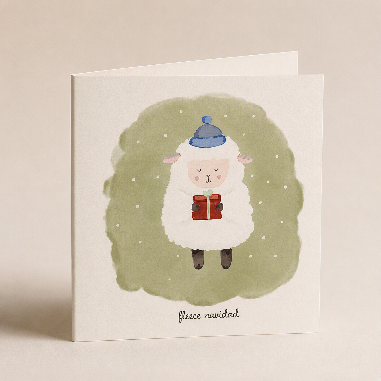 Square Christmas card featuring a cute sheep in a blue hat holding a gift on a sage green watercolor background.