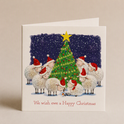 Square Christmas card featuring a flock of sheep in Santa hats gathered around a decorated tree on a snowy night.