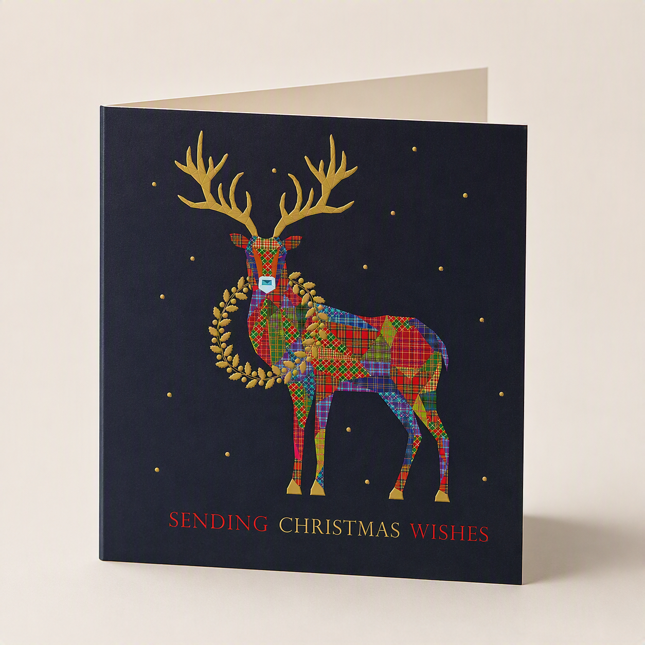 Square Christmas card with a tartan stag, gold antlers, and holly wreath on a dark blue background with festive text.