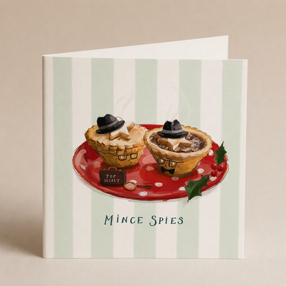 Square Christmas card featuring two mince pies dressed as spies with hats and glasses on a red plate, striped background.