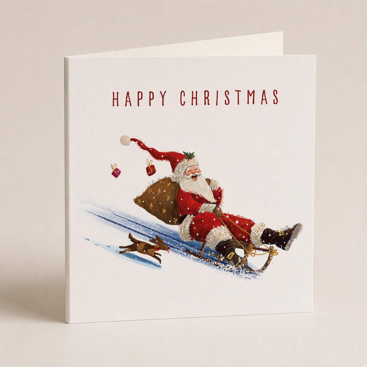 Square Christmas card featuring a joyful Santa sledding with a dog, satin finish, 140mm size, with Happy Christmas text.
